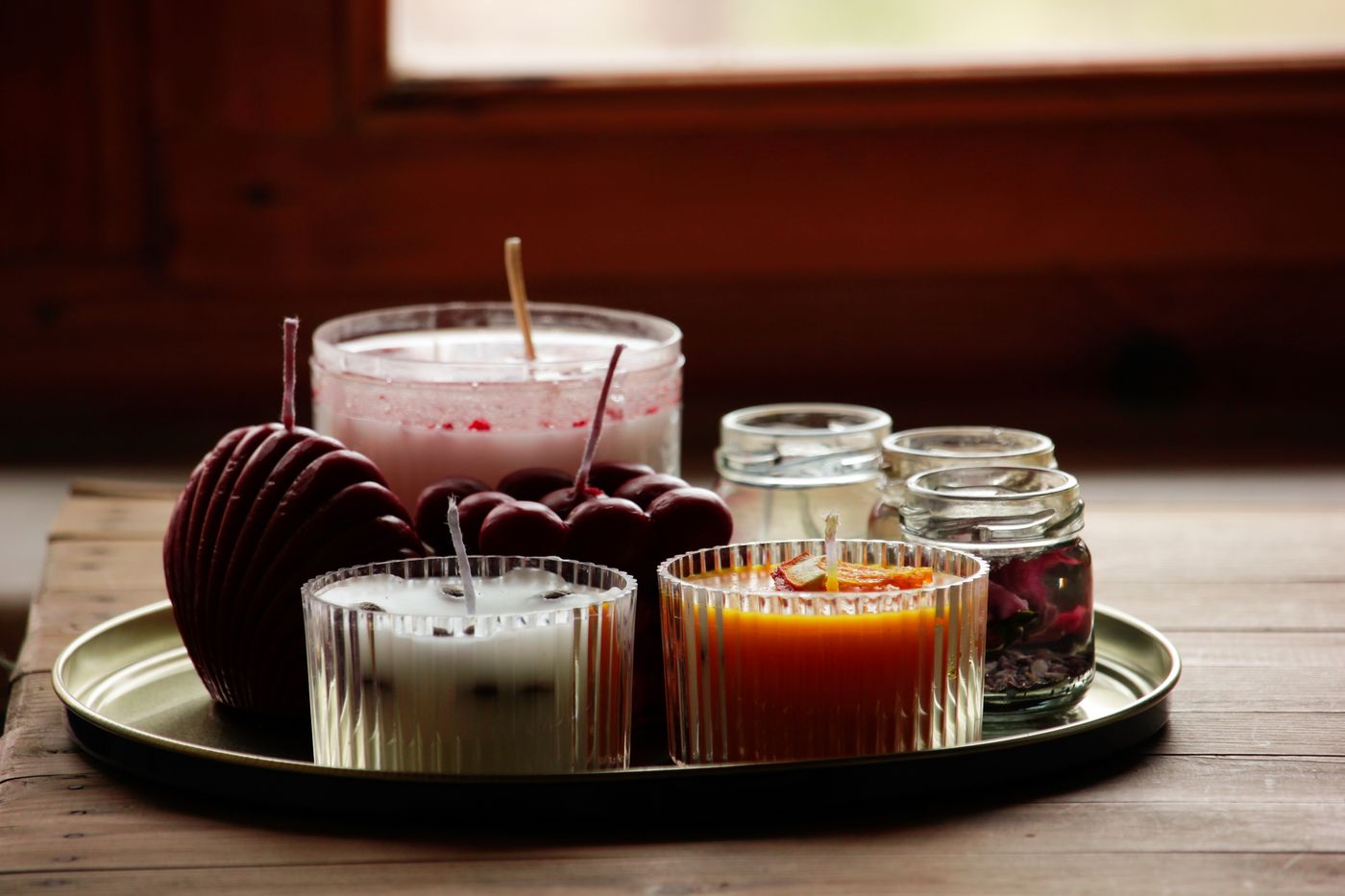 Hand-poured candles in glass jars on a tray by a window