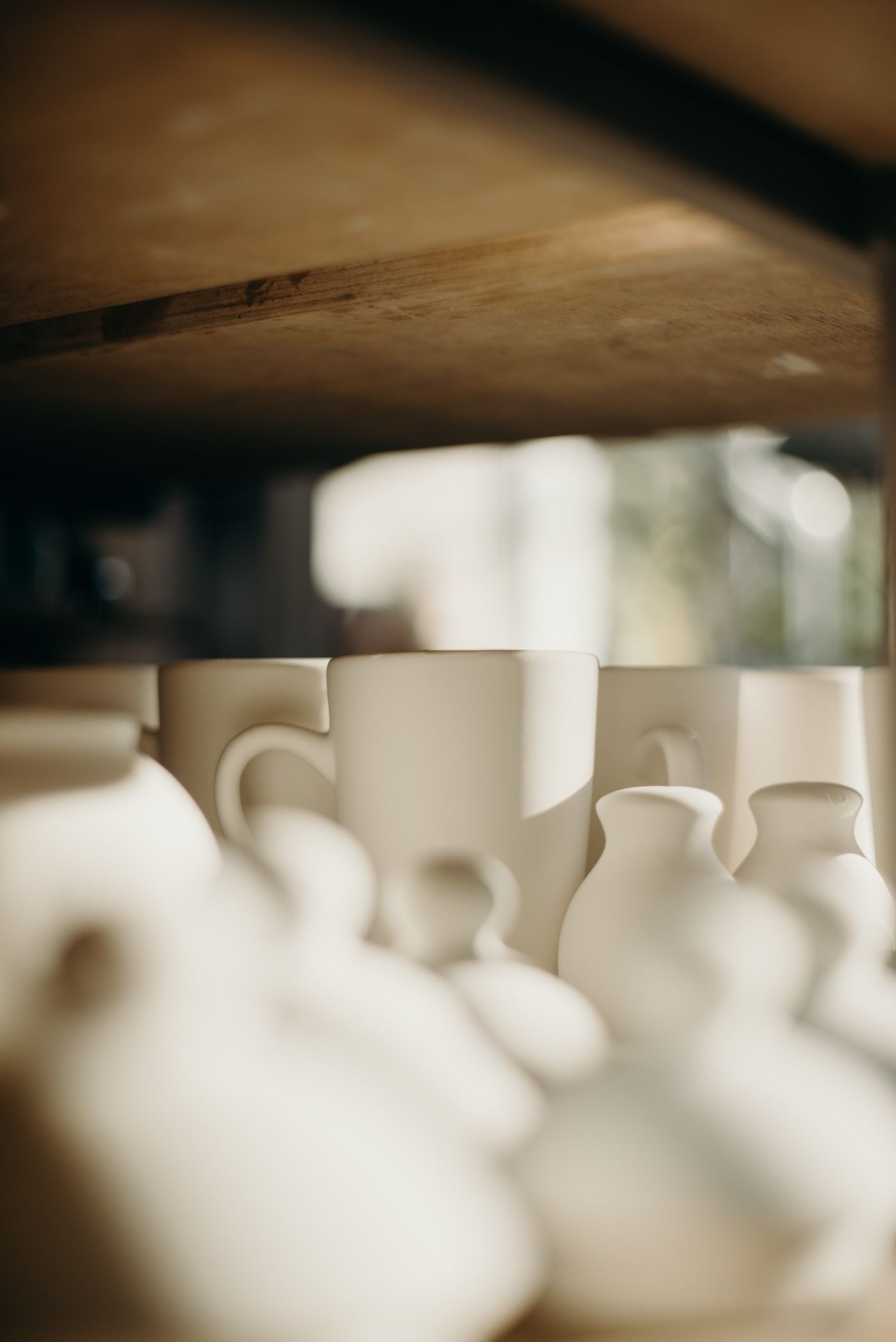 Creamy handmade ceramic mugs and small vases on a wooden shelf