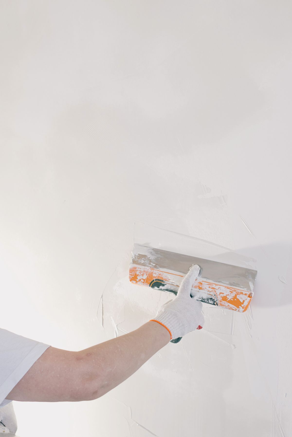 A wide finishing trowel skimming a smooth coat across a drywall wall