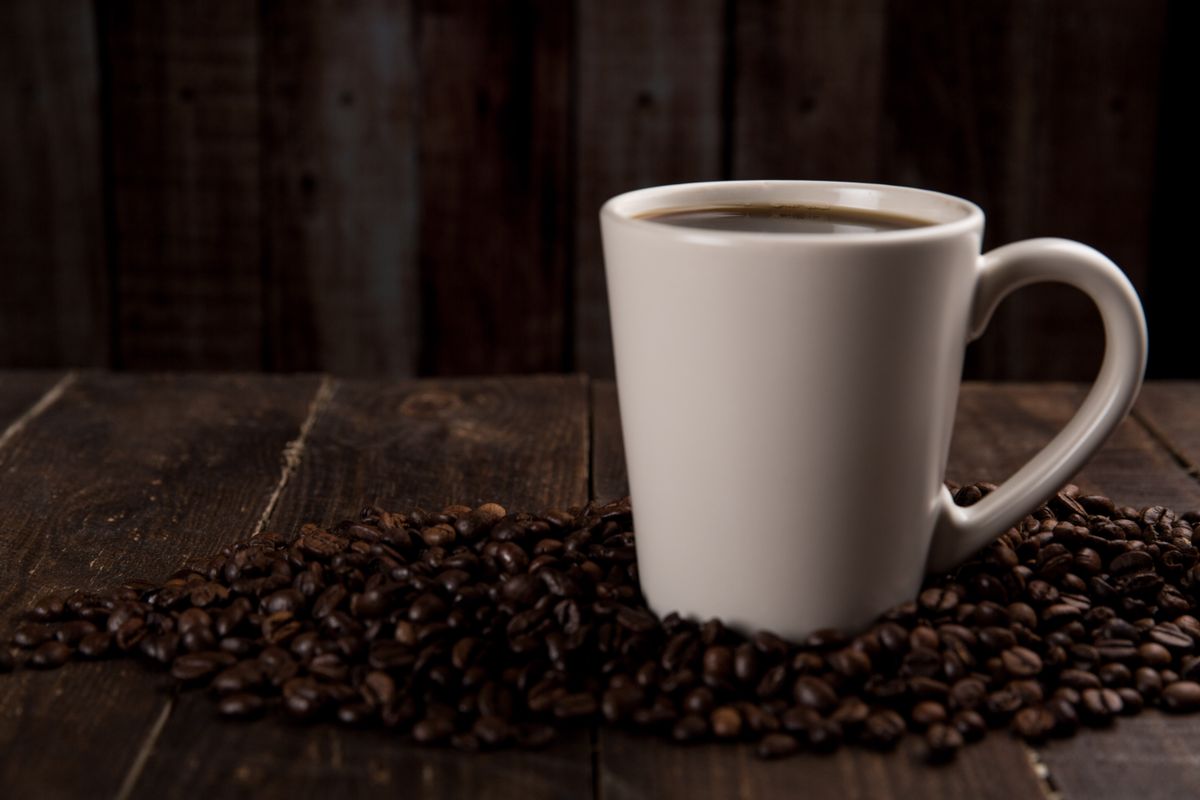 A cup of black coffee beside roasted beans on dark wood