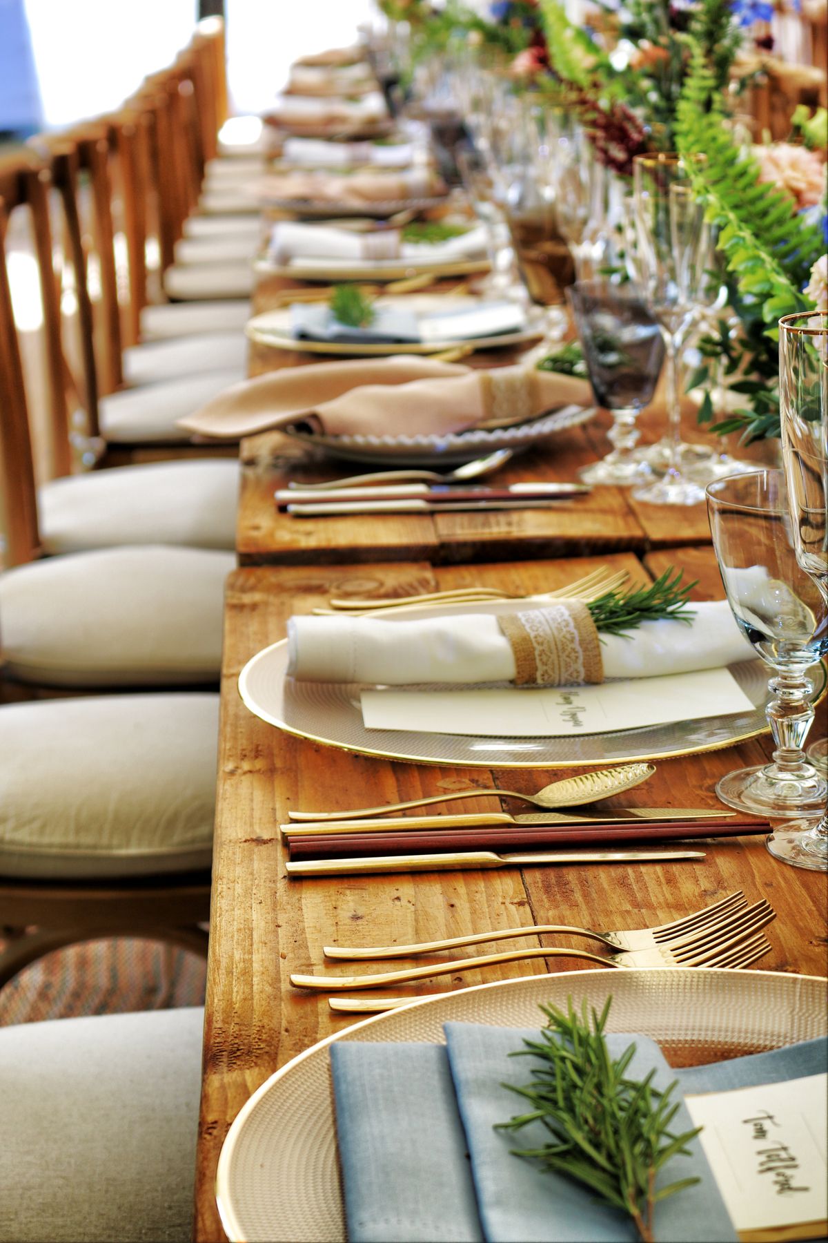 A long catering table set with linens, glassware and rosemary