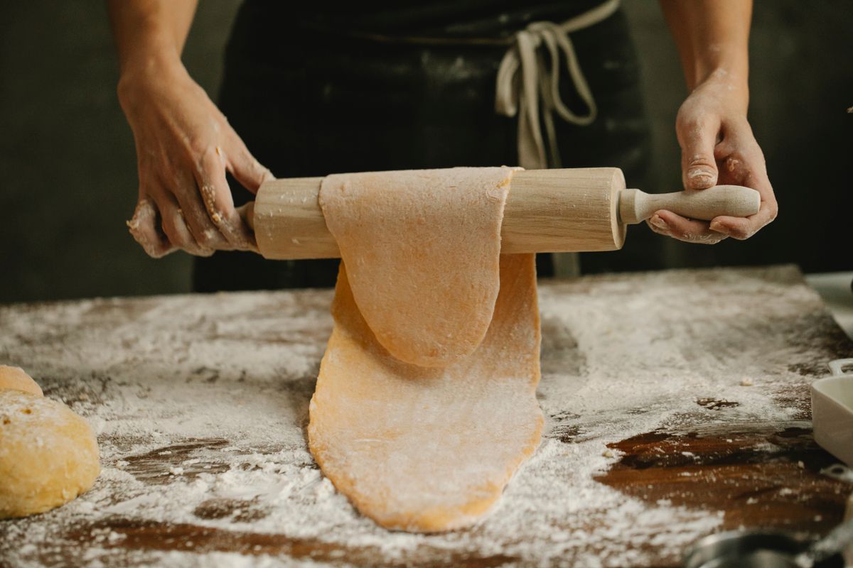 Hands rolling fresh pasta dough with a rolling pin