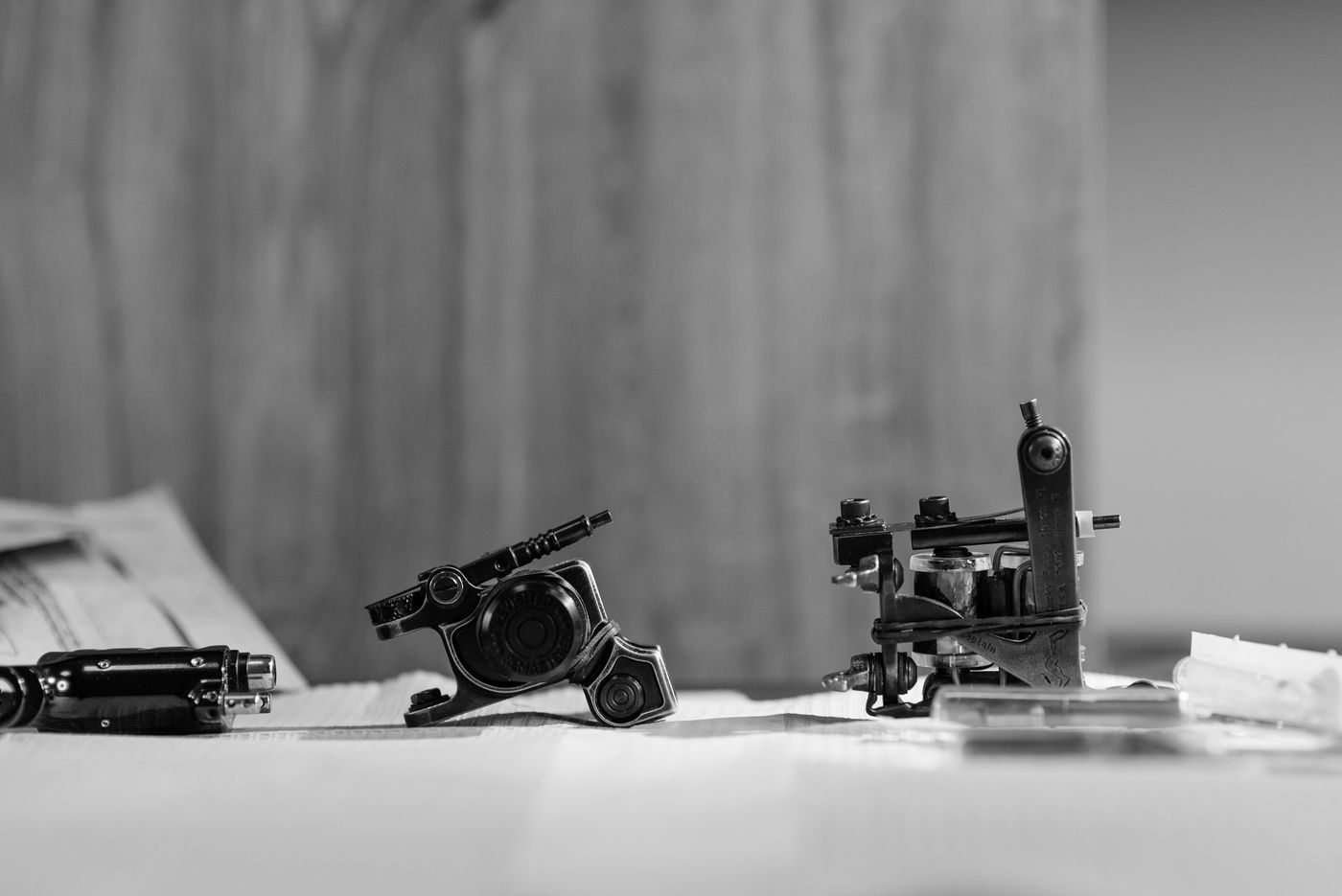 Tattoo machines resting on a surface, in black and white