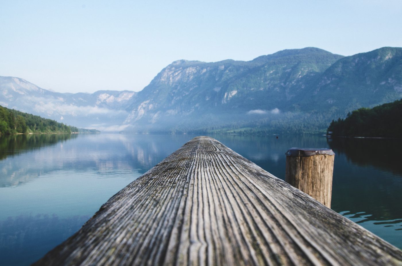 A wooden dock leading into a calm, mountain-ringed cove