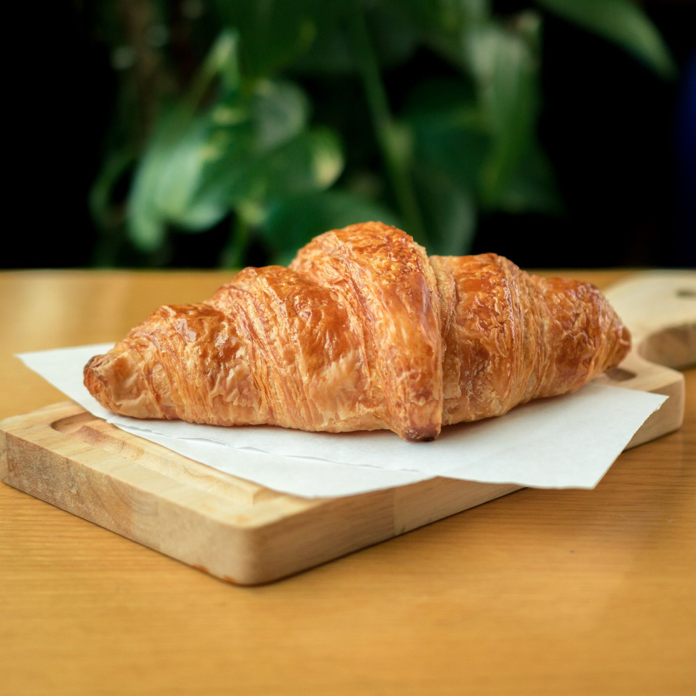 A golden flaky croissant on a wooden board