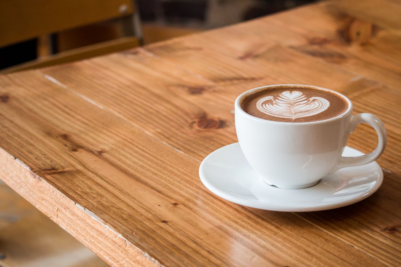 A white cup with latte art on a warm wooden table