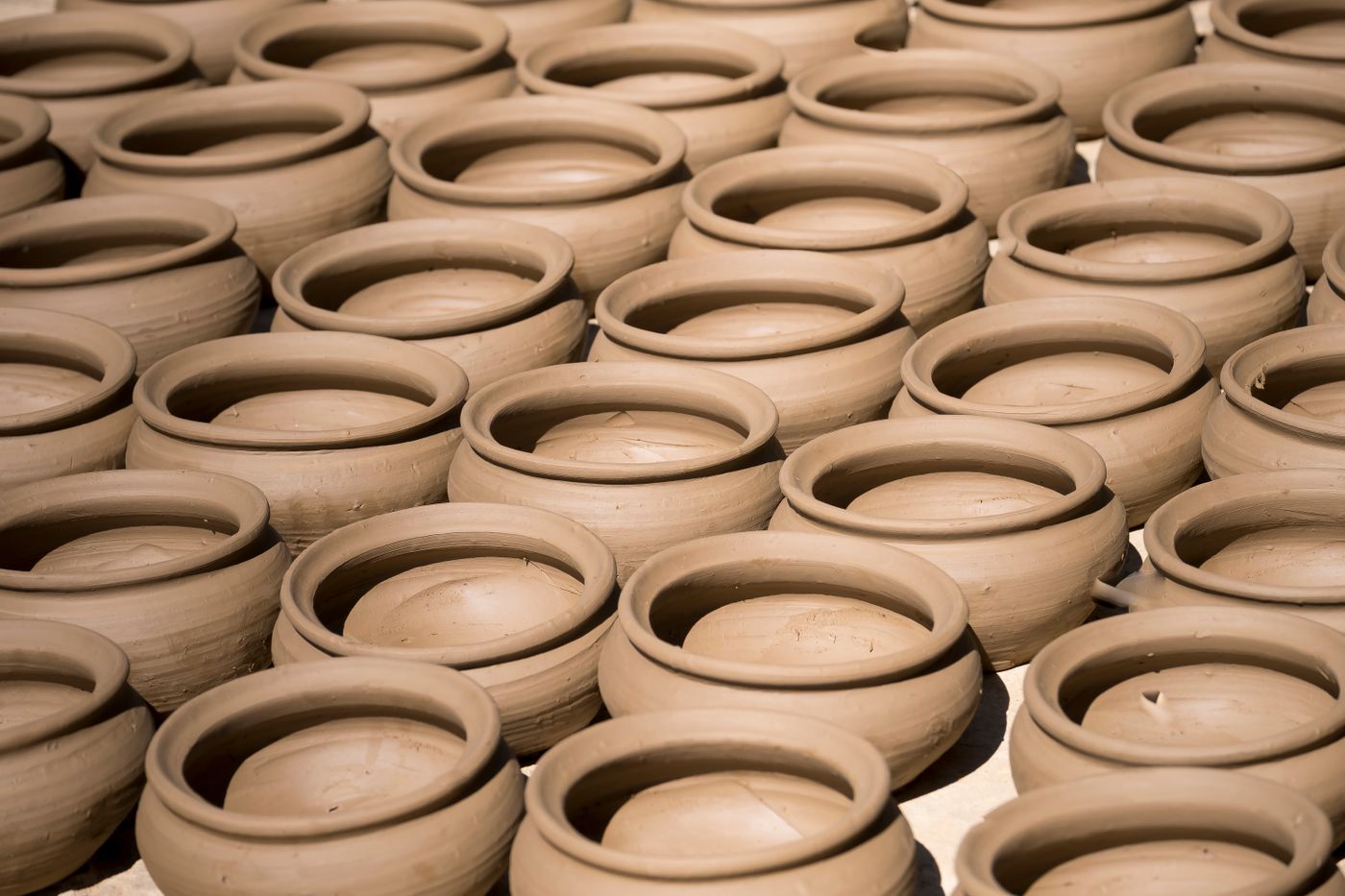 Rows of raw clay bowls drying on a rack