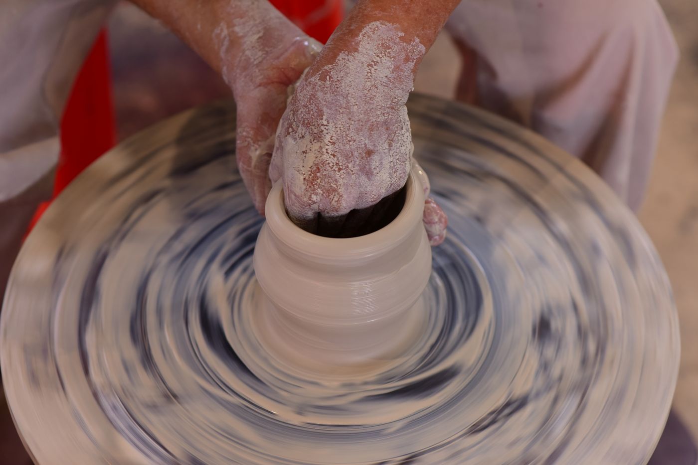 Clay-covered hands pulling a tall vessel on a spinning wheel