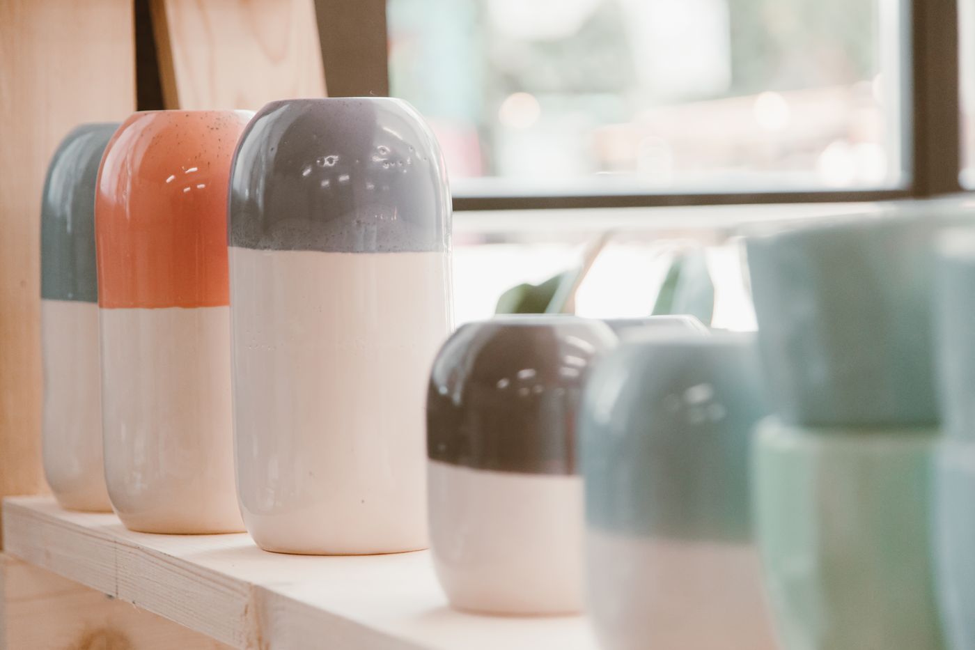 Two-tone ceramic vases lined on a wooden shelf