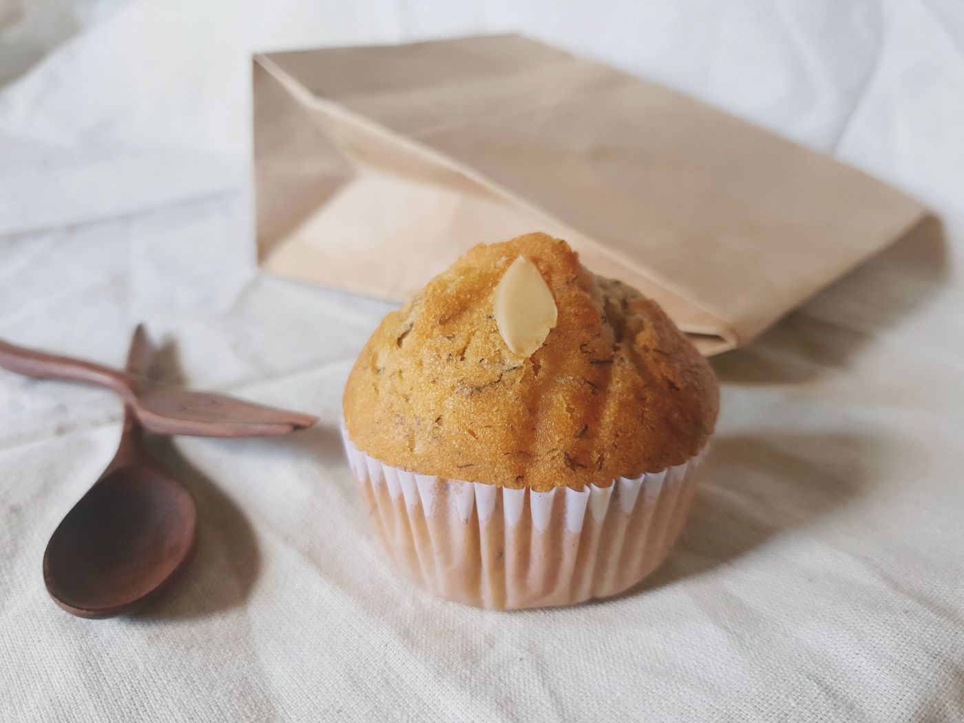 A single almond-topped muffin with a paper bag
