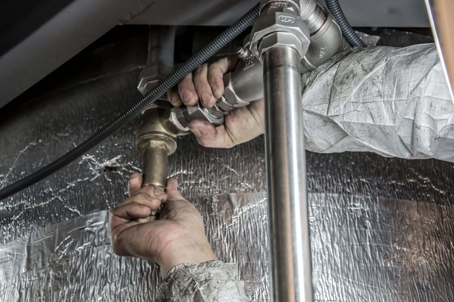 Hands fitting an insulated line on ductwork with a wrench