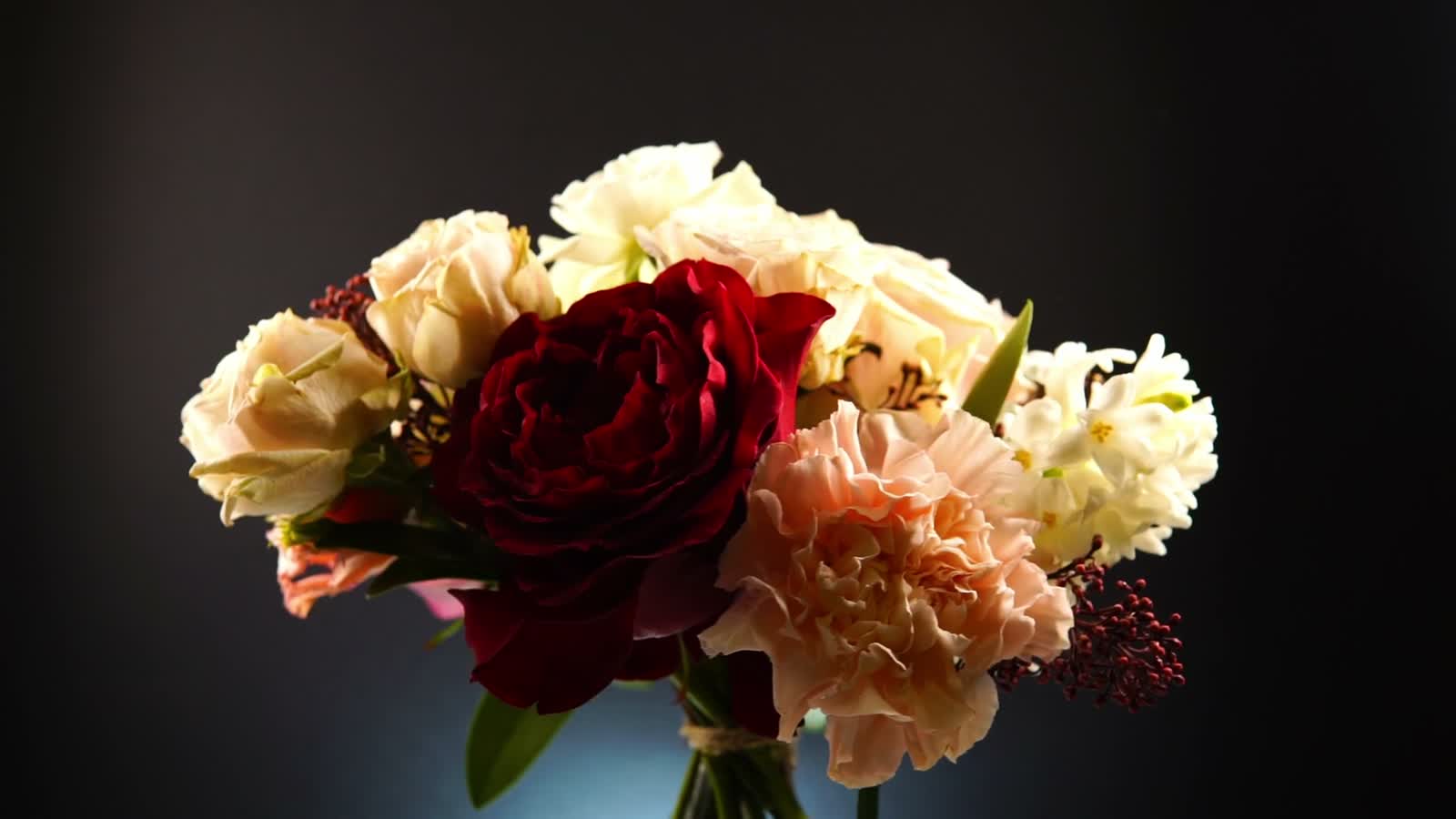 A hand-tied bouquet of roses and carnations lit against a dark backdrop