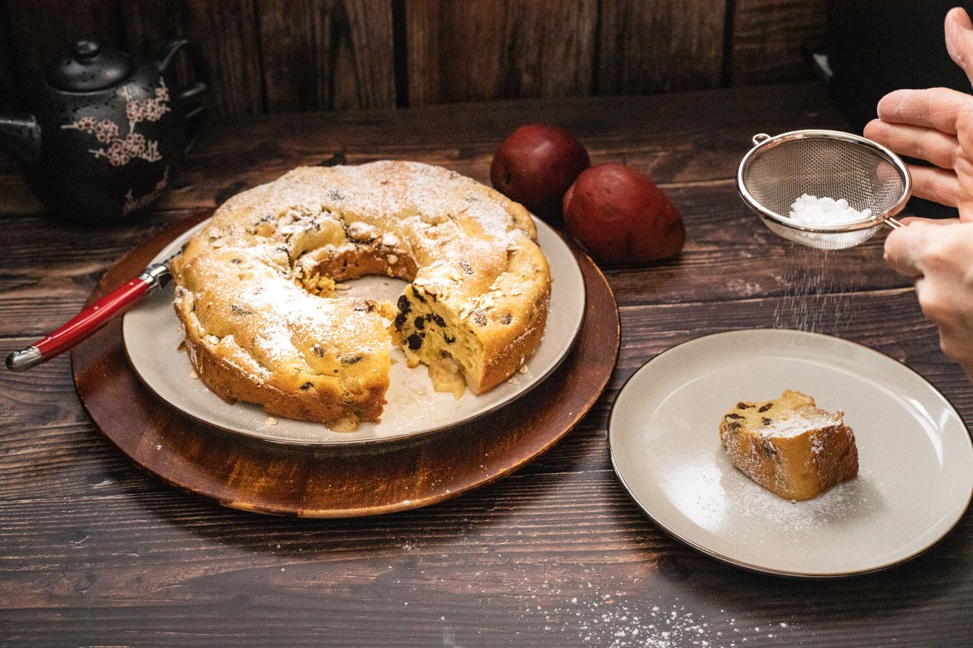 A dusted ring cake with sugar being sifted over the top by hand