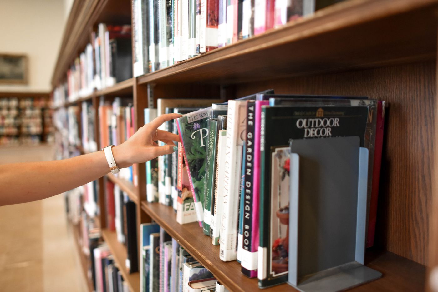 A hand reaching for a book on a wooden bookshelf