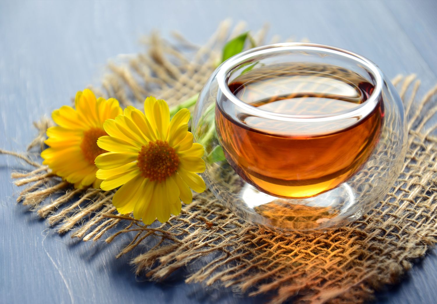 A glass of amber loose-leaf tea on a woven mat