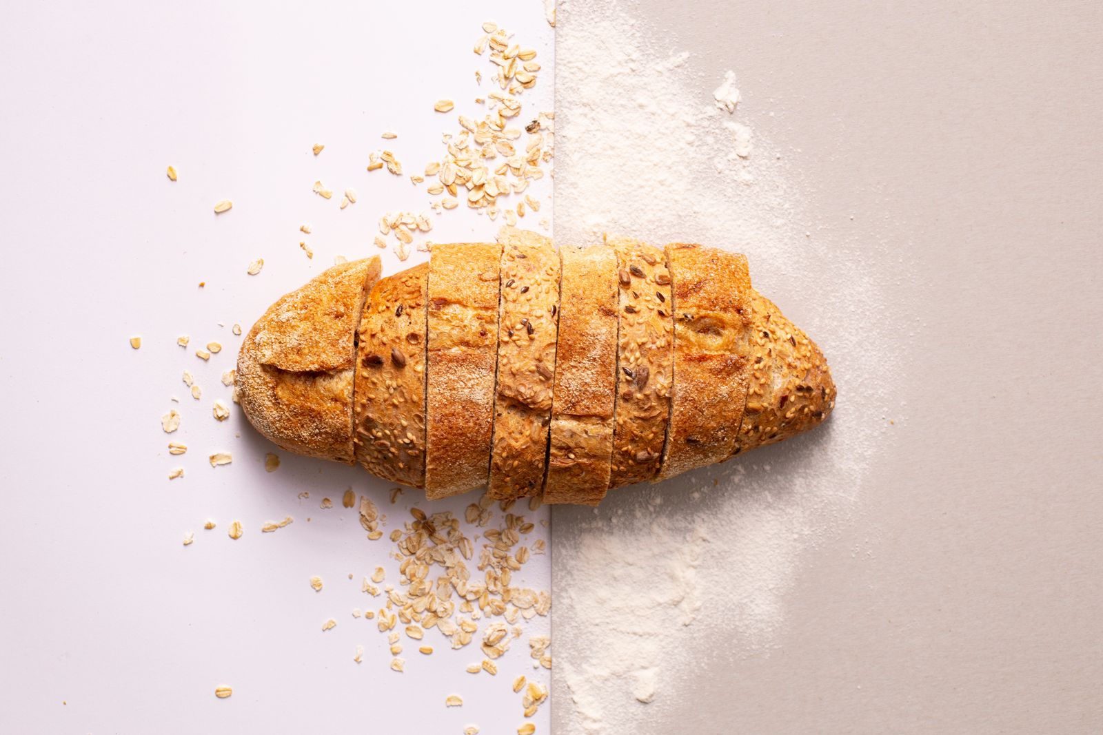 A seeded loaf sliced on the bench, dusted with oats and flour